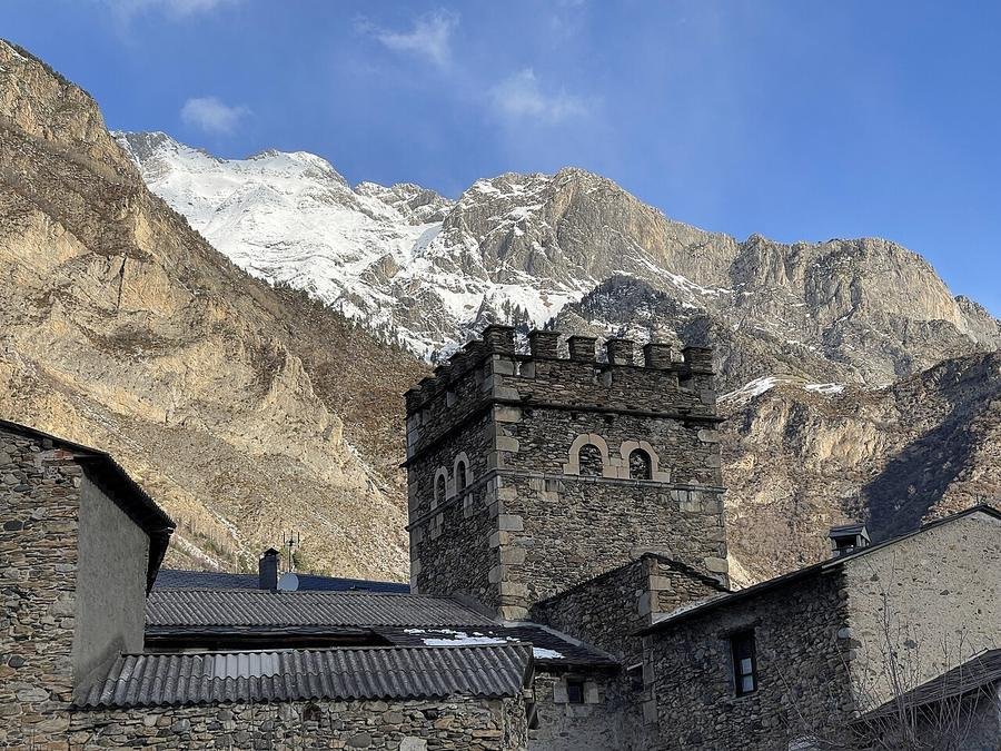 Torreón de piedra entre tejados de pizarra en Benasque con montañas nevadas